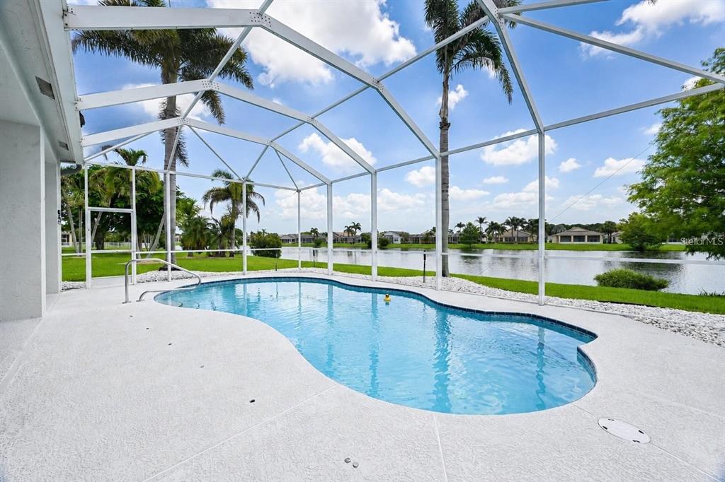 A swimming pool enclosed by a screened lanai overlooks a lake and residential neighborhood — 468 SW TALQUIN LANE, PORT ST LUCIE, FL