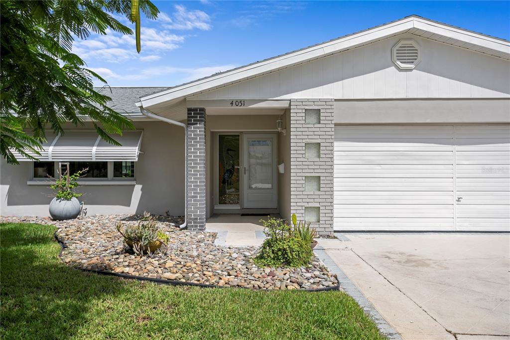 The exterior of a single-story house features a brick-accented entryway, a garage, and rock landscaping — 4051 14TH STREET NE, ST PETERSBURG, FL
