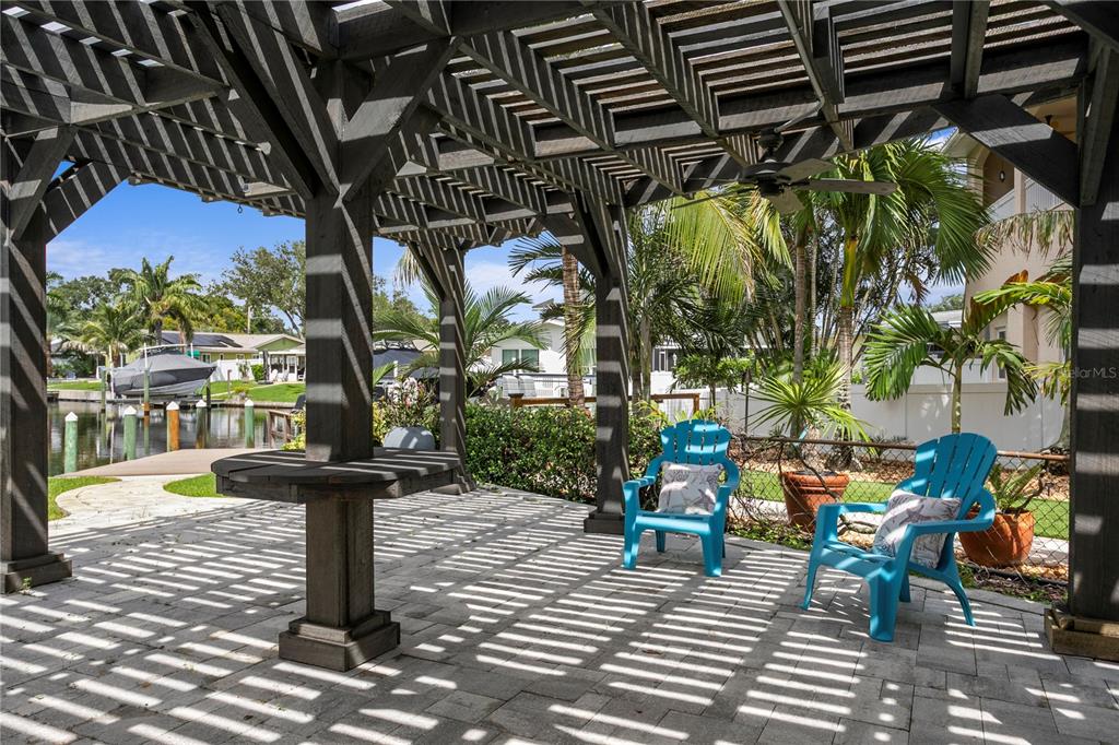 A paved patio features a wooden pergola, two blue Adirondack chairs, and a waterfront view — 4051 14TH STREET NE, ST PETERSBURG, FL