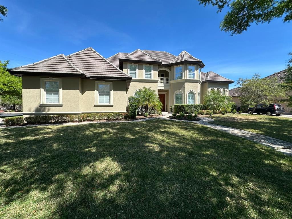 A two-story house with a tan stucco exterior, dark tile roof, and a front lawn — 8734 CRESTGATE CIRCLE, ORLANDO, FL