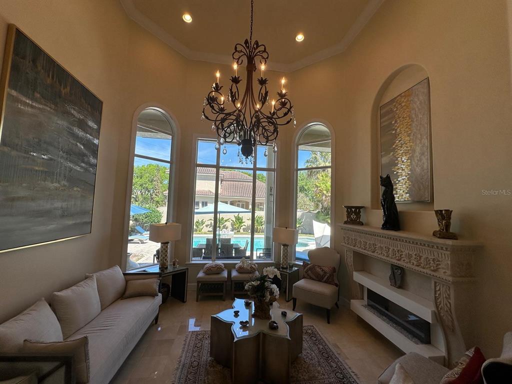 A living room features a high ceiling, a large chandelier, a fireplace, and pool views — 8734 CRESTGATE CIRCLE, ORLANDO, FL