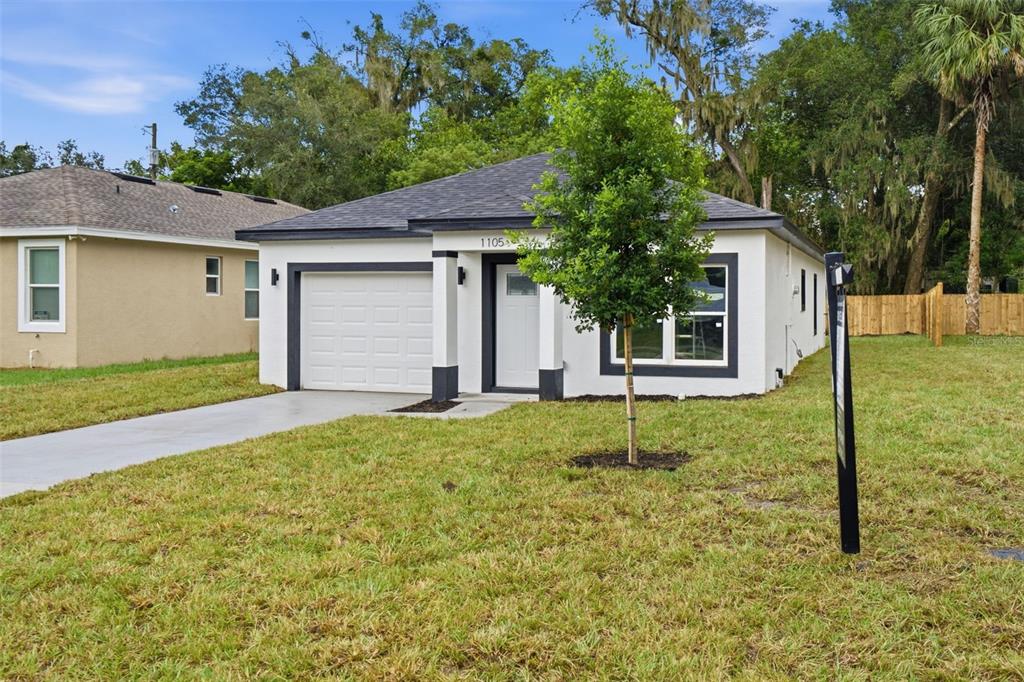 A single-story white house with a dark roof, a garage, and a small front yard — 1105 S ADELLE AVENUE, DELAND, FL