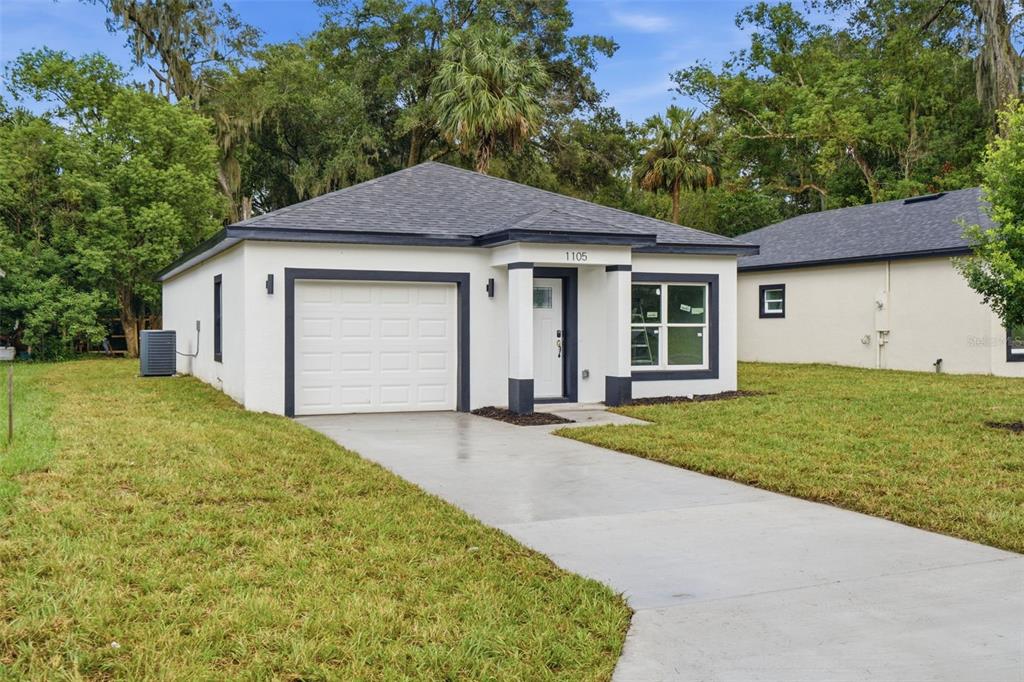 A single-story white house with a dark roof, a one-car garage, and a concrete driveway — 1105 S ADELLE AVENUE, DELAND, FL