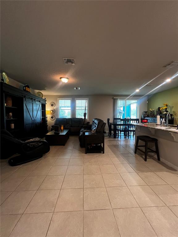 A tiled hallway leads toward a living room with windows and a dark sofa — 17268 CAGAN CROSSINGS BOULEVARD, CLERMONT, FL