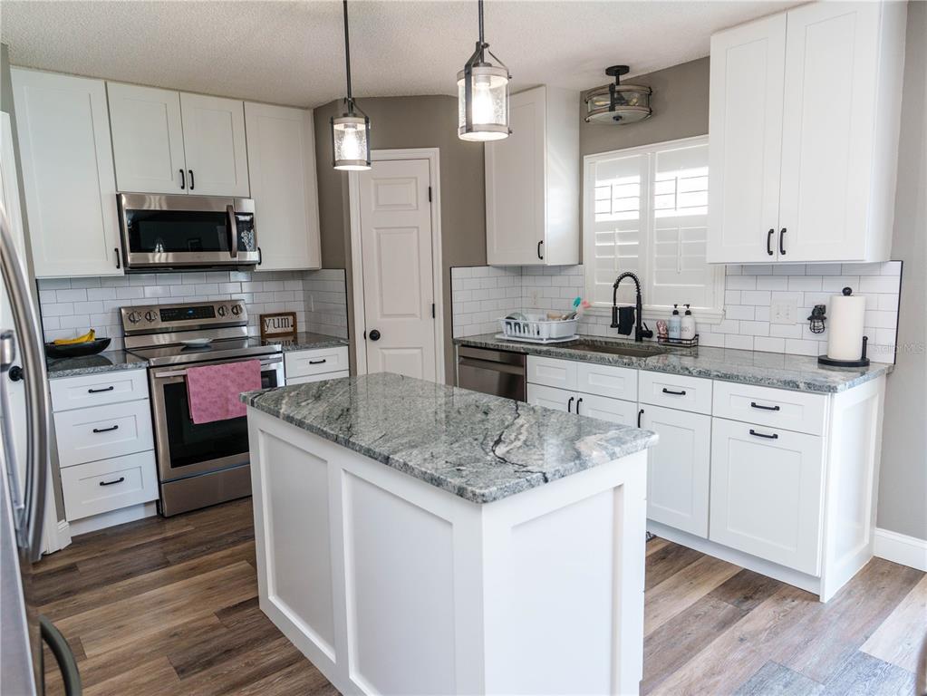 A kitchen features white cabinets, granite countertops, a central island, and stainless steel appliances — 2722 HEATHGATE WAY, LAND O LAKES, FL