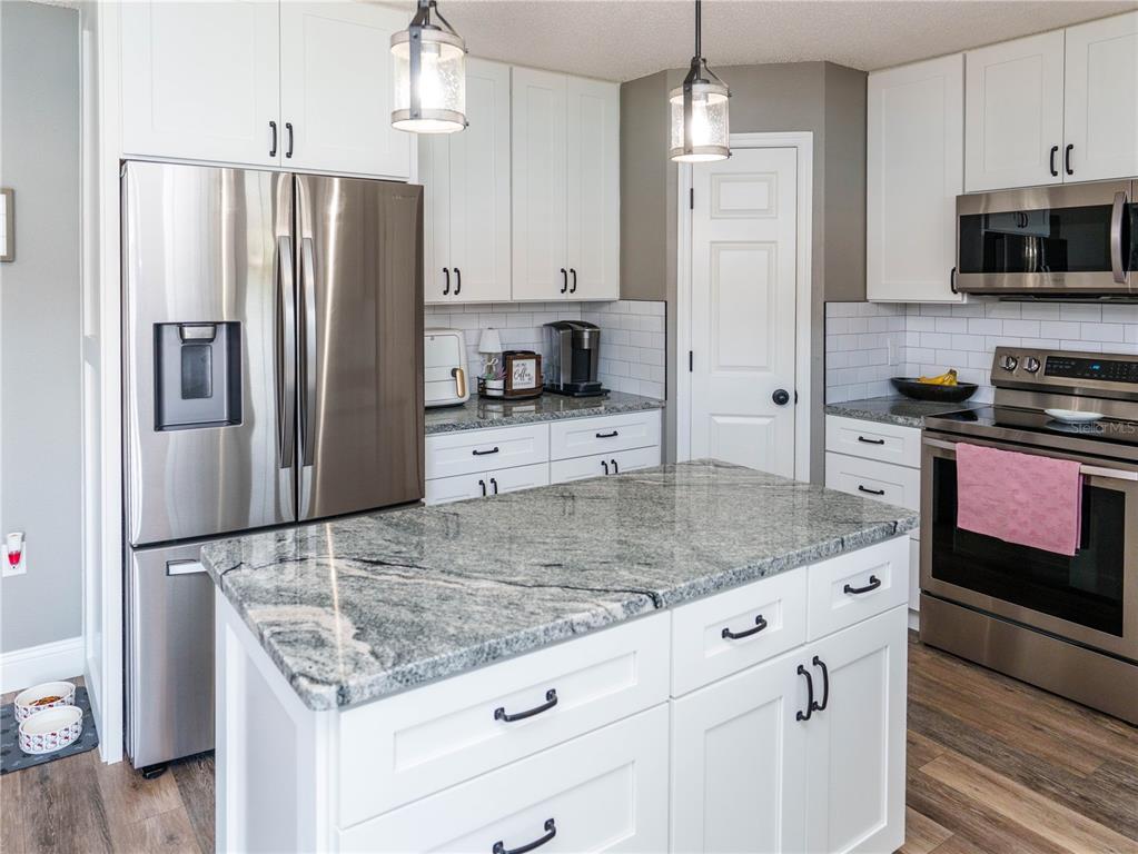 A kitchen features white cabinets, granite countertops, stainless steel appliances, and a central island — 2722 HEATHGATE WAY, LAND O LAKES, FL
