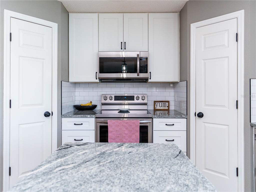 A kitchen features white cabinets, stainless steel appliances, granite countertops, and a subway tile backsplash — 2722 HEATHGATE WAY, LAND O LAKES, FL