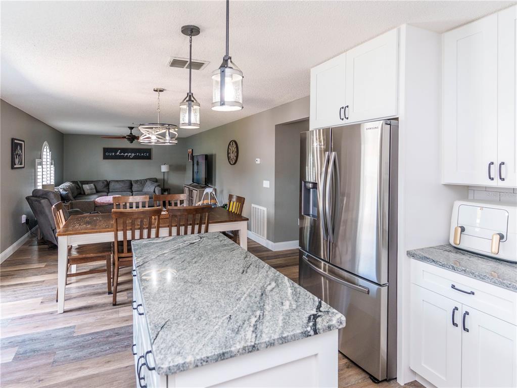 A kitchen with white cabinets and granite countertops overlooks an open-concept dining and living area — 2722 HEATHGATE WAY, LAND O LAKES, FL