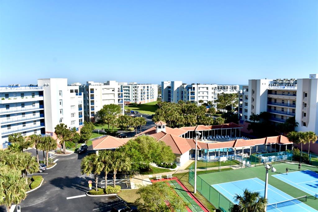 An aerial view shows apartment buildings, a swimming pool, and tennis courts on a sunny day — 5300 S ATLANTIC AVENUE UNIT 8-402, NEW SMYRNA BEACH, FL