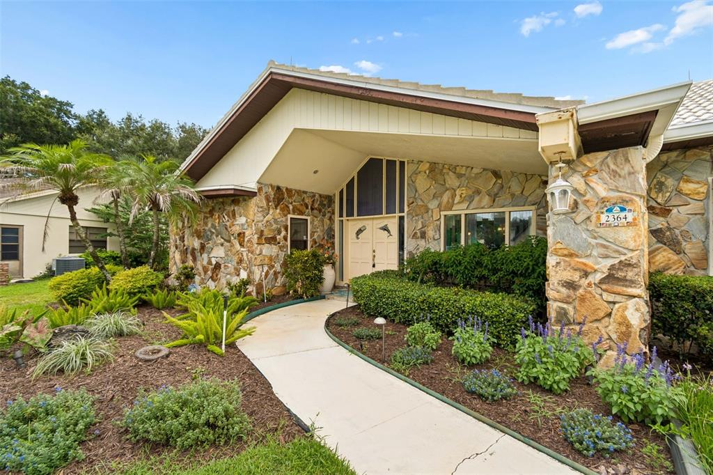 A stone-faced house exterior features a curved walkway leading to double front doors — 2364 VIOLET PL, PALM HARBOR, FL