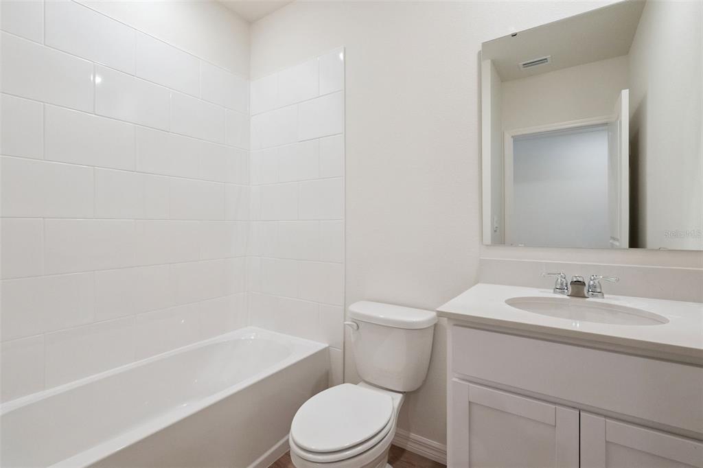 A bathroom features a white bathtub with tiled walls, a toilet, and a vanity sink — 1340 FOUNTAIN VIEW STREET, ORMOND BEACH, FL