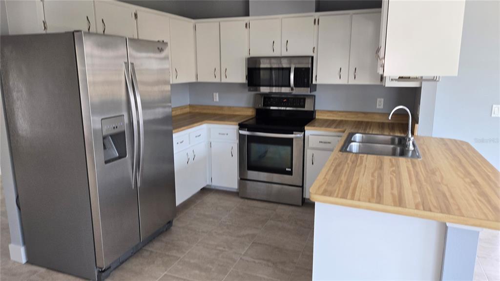 A kitchen features white cabinets, stainless steel appliances, and wood-look laminate countertops — 347 HOLLY ROAD, VENICE, FL