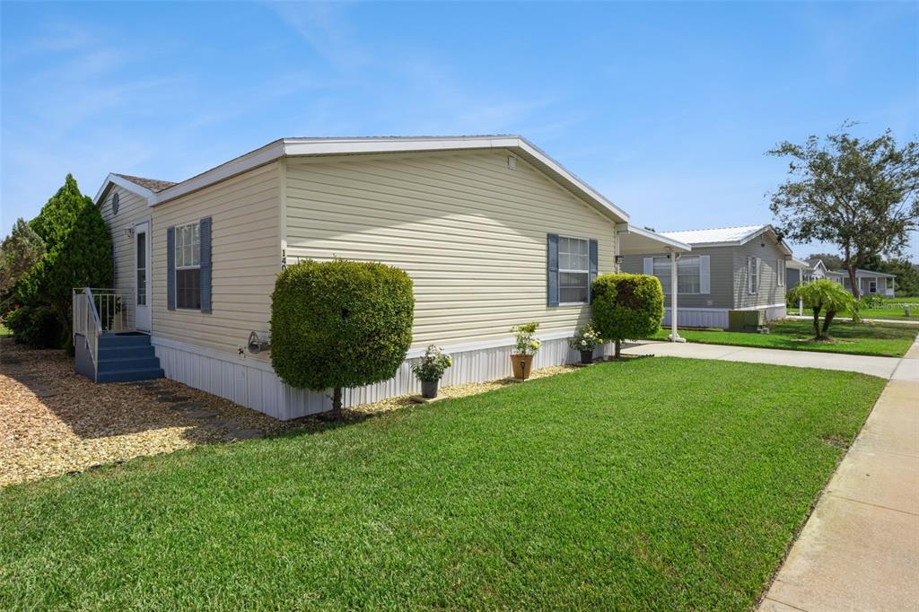 A light yellow manufactured home with blue shutters sits on a grassy lot — 14019 ROYAL FERN WAY, ASTATULA, FL