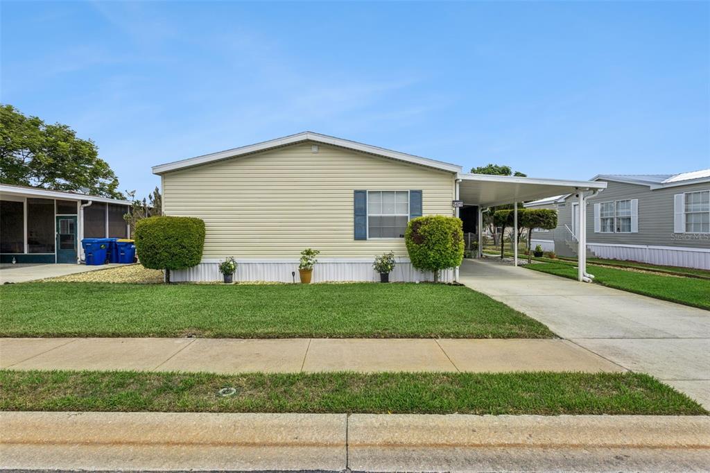 A single-story manufactured home with light yellow siding, a carport, and a front lawn — 14019 ROYAL FERN WAY, ASTATULA, FL