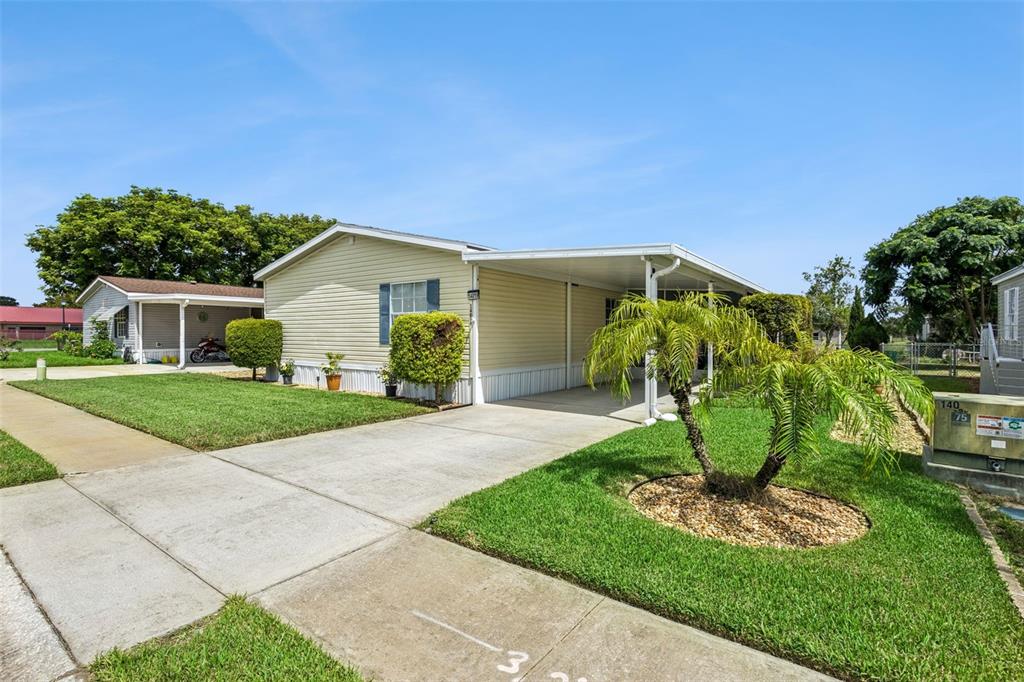 A light yellow manufactured home features a concrete driveway, a carport, and a small palm tree — 14019 ROYAL FERN WAY, ASTATULA, FL