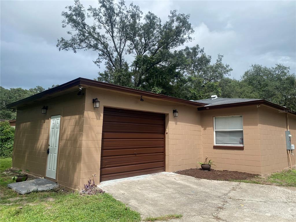 A tan concrete block garage with a brown roll-up door and a white side door — 1608 LONG LANE, APOPKA, FL