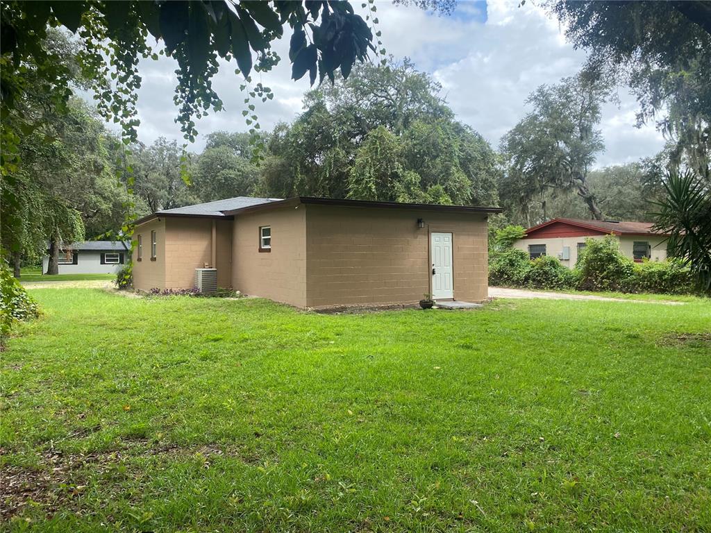 A tan concrete block building sits on a grassy lot with trees in the background — 1608 LONG LANE, APOPKA, FL