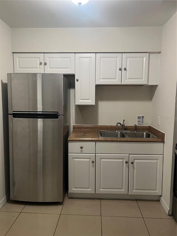 A small kitchen features white cabinets, a stainless steel refrigerator, and a brown laminate countertop — 1608 LONG LANE, APOPKA, FL