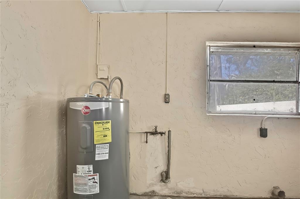 A Rheem water heater is installed against a textured wall next to a window — 12130 MAPLE STREET, DUNNELLON, FL