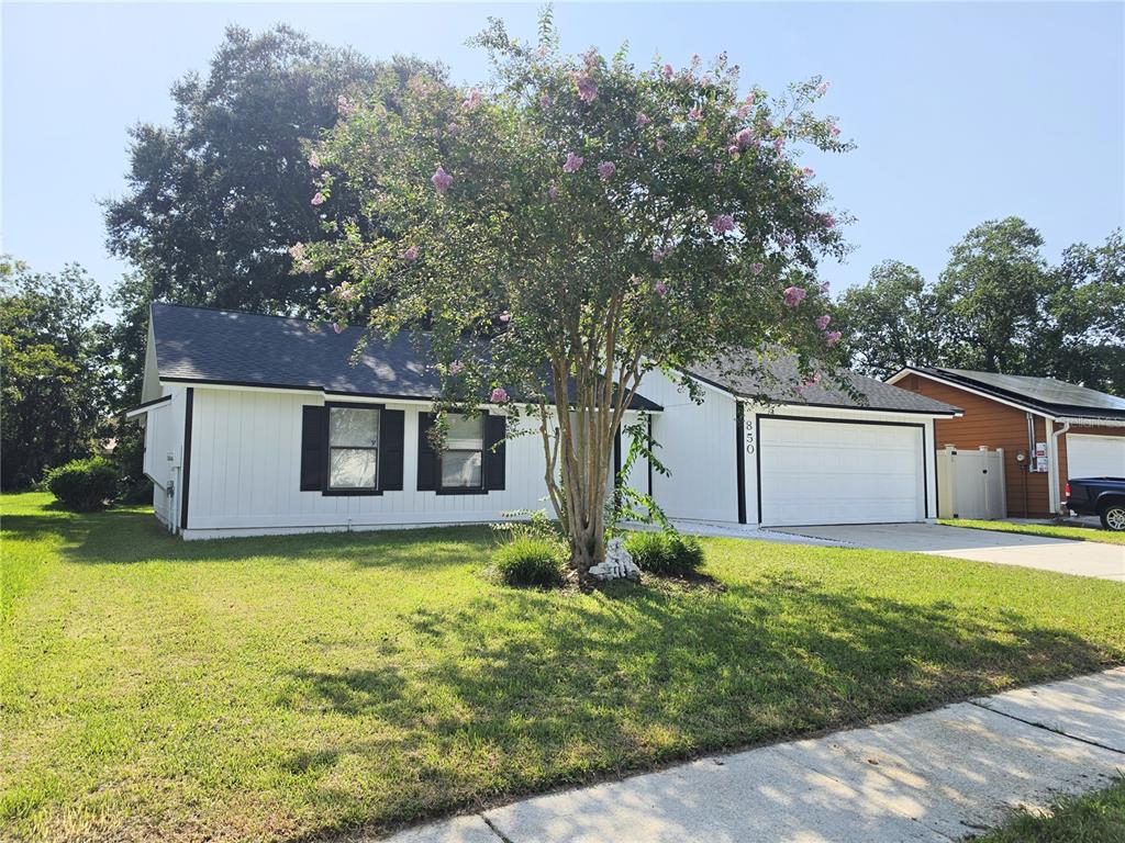 A white single-story house with black shutters and a two-car garage sits behind a tree — 850 ARIES ROAD W, JACKSONVILLE, FL