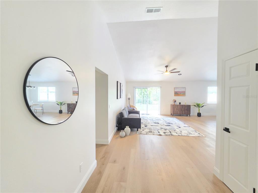 A bright, open-concept living area features light wood floors, a round wall mirror, and sliding doors — 850 ARIES ROAD W, JACKSONVILLE, FL
