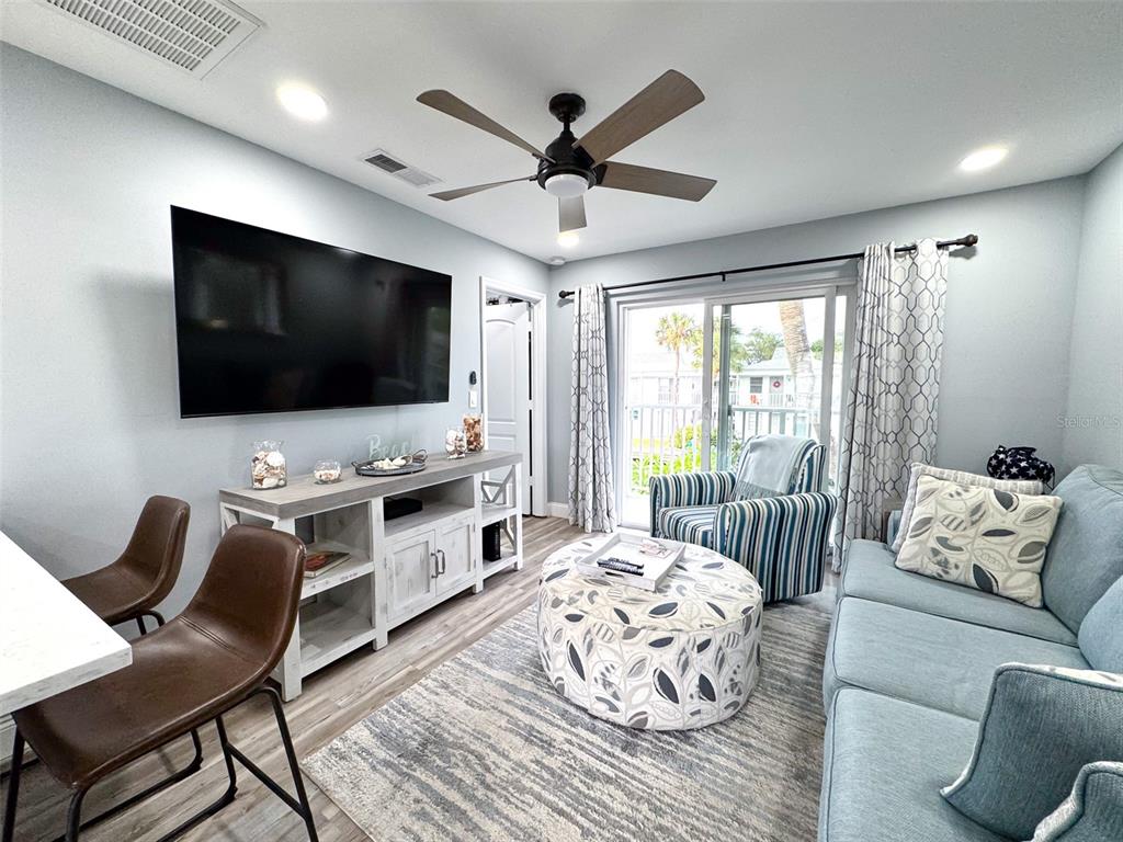 A living room features a television, a ceiling fan, a sofa, and a sliding glass door — 902 GIBBS ROAD UNIT 283, VENICE, FL