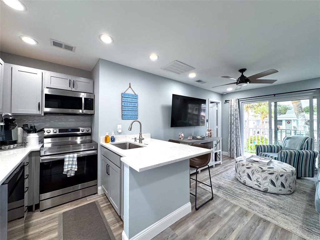 A kitchen with gray cabinets and white countertops opens into a living area with furniture — 902 GIBBS ROAD UNIT 283, VENICE, FL