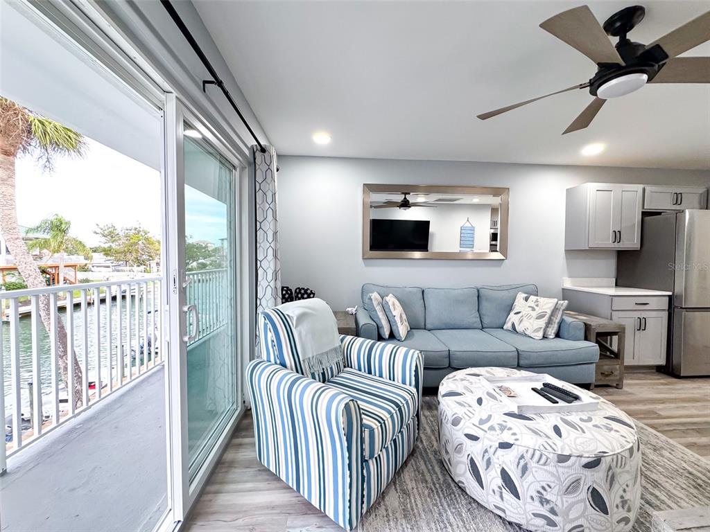 A living room features a blue sofa, striped armchair, patterned ottoman, and a balcony view — 902 GIBBS ROAD UNIT 283, VENICE, FL