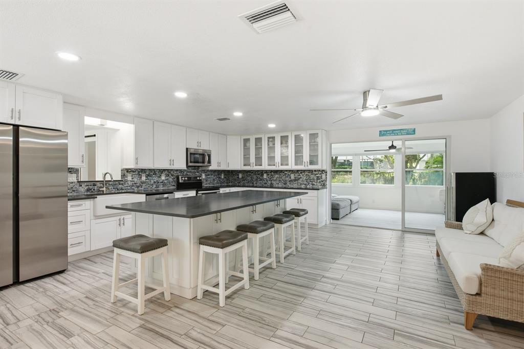 A modern kitchen features white cabinetry, a large dark island, and tile flooring — 601 SHORE DRIVE E, OLDSMAR, FL