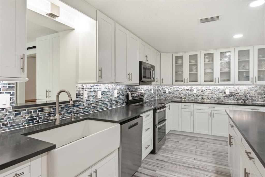 A kitchen with white cabinets, dark countertops, a farmhouse sink, and a blue tiled backsplash — 601 SHORE DRIVE E, OLDSMAR, FL