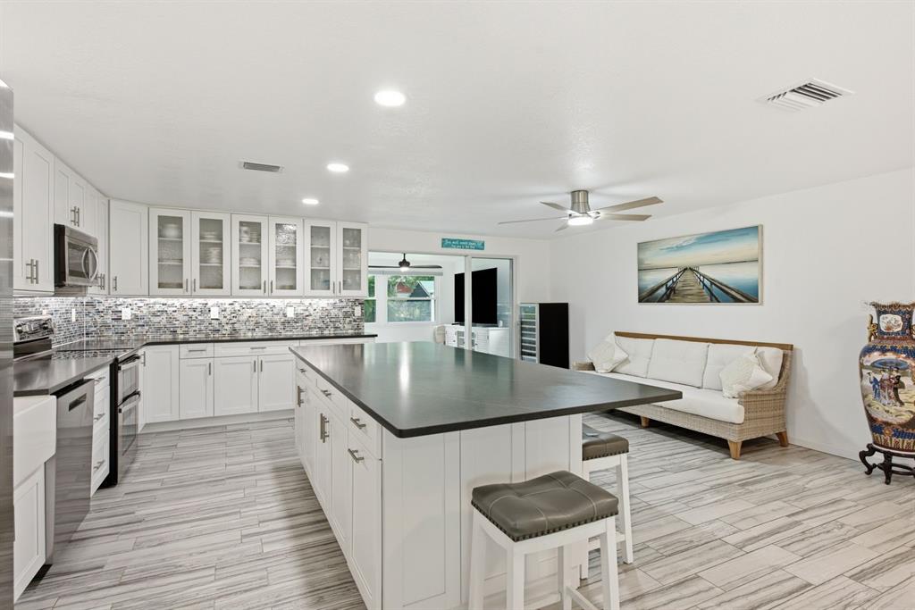 A modern kitchen features white cabinetry, a large dark island, and light wood-look tile flooring — 601 SHORE DRIVE E, OLDSMAR, FL