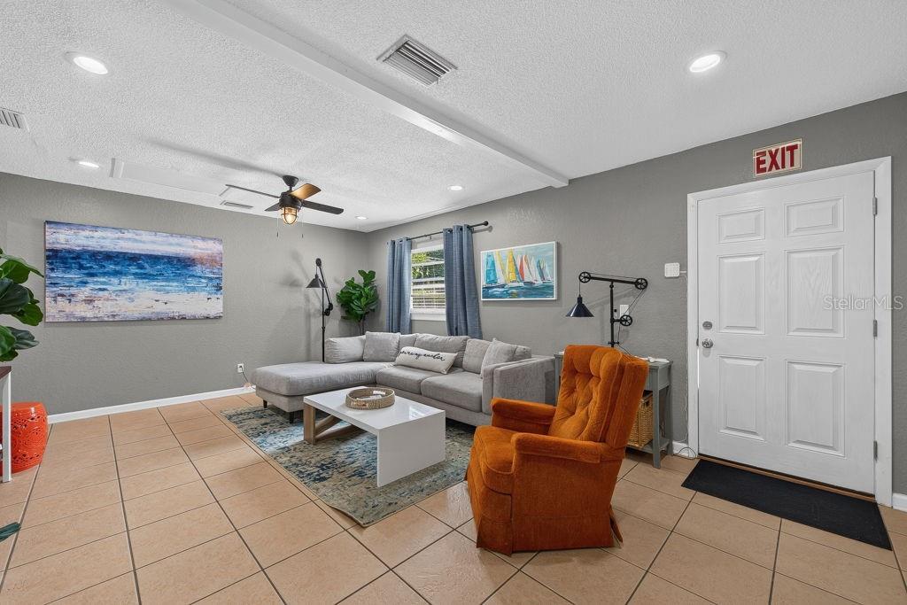 A living room features a grey sectional sofa, an orange armchair, and tile flooring — 610 1ST AVENUE NE, LARGO, FL