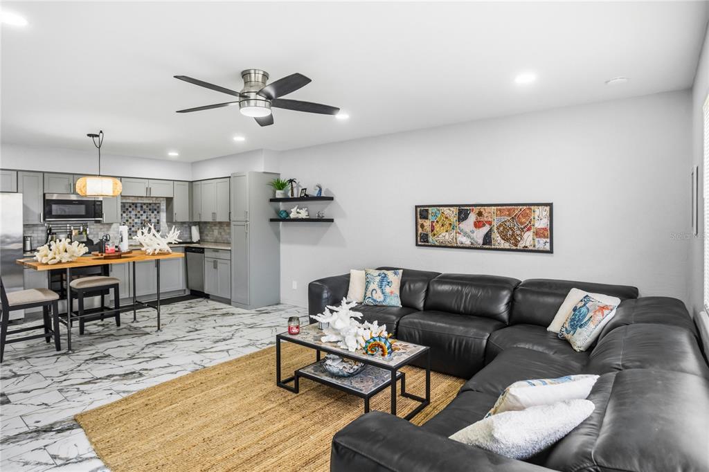 An open-concept living room and kitchen featuring gray cabinetry, a black sectional, and marble flooring — 416 73RD AVENUE N UNIT 207, ST PETERSBURG, FL