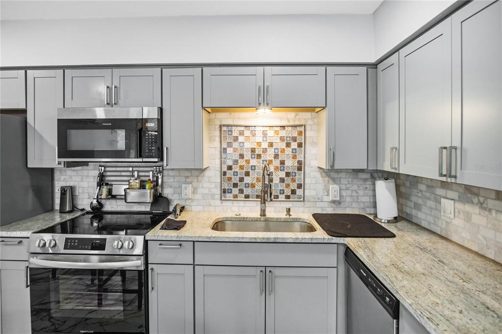 A kitchen features gray cabinets, stainless steel appliances, a tiled backsplash, and granite countertops — 416 73RD AVENUE N UNIT 207, ST PETERSBURG, FL