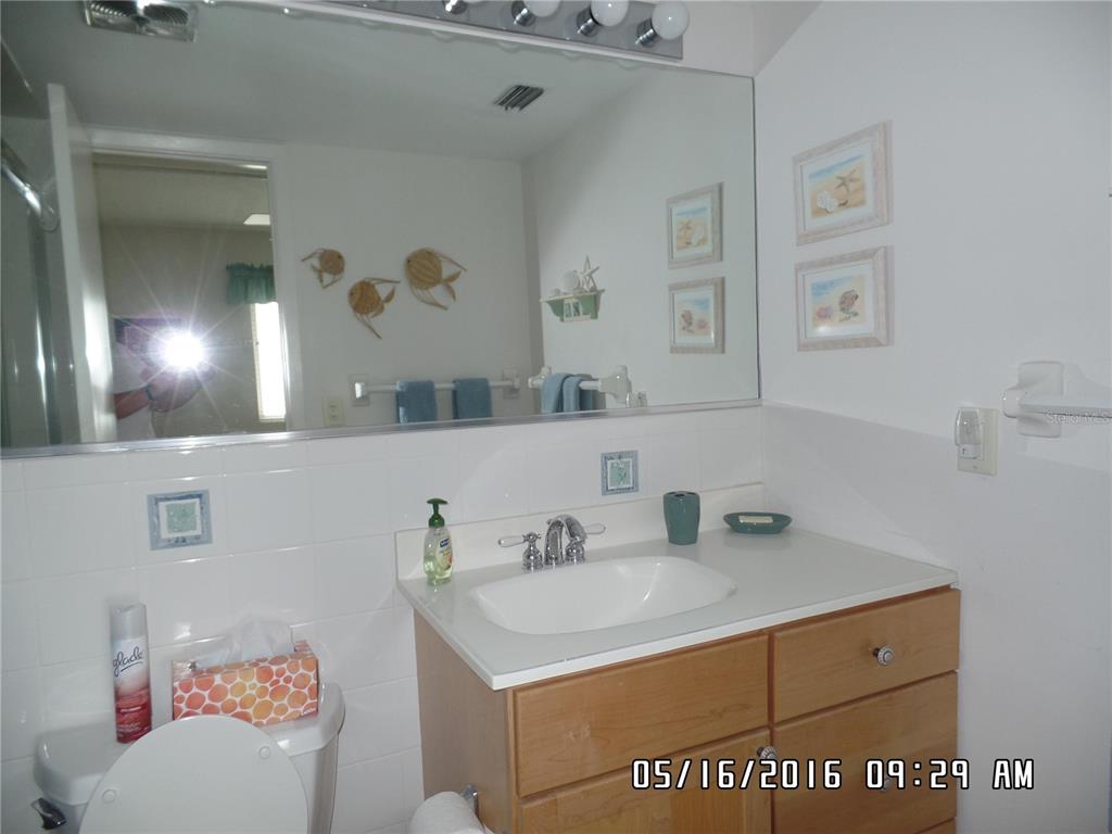 A bathroom features a wooden vanity with a white sink, a large mirror, and white tiles — 815 OCEAN SHORE BOULEVARD UNIT 9A, ORMOND BEACH, FL