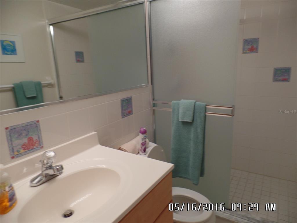 A bathroom features a white vanity, a mirror, and a glass-enclosed shower with tiled walls — 815 OCEAN SHORE BOULEVARD UNIT 9A, ORMOND BEACH, FL