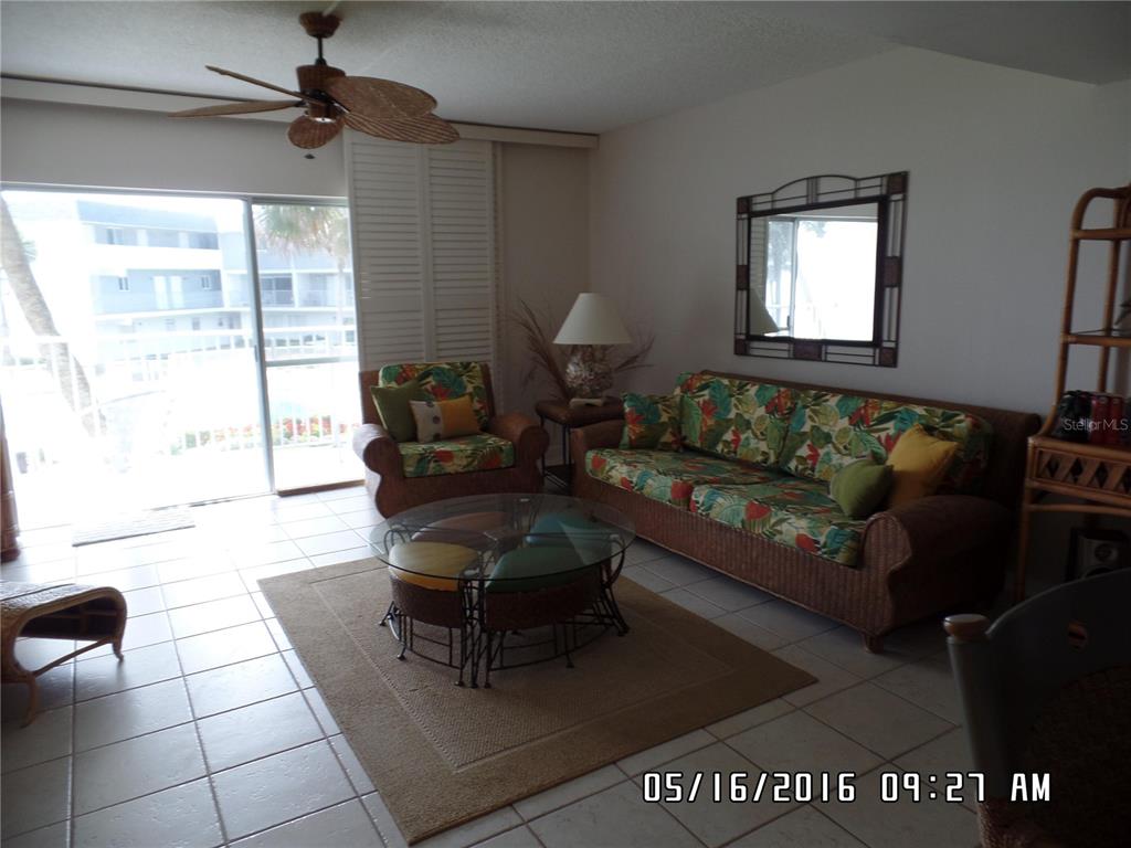 A living room features wicker furniture with tropical cushions, a glass coffee table, and tile flooring — 815 OCEAN SHORE BOULEVARD UNIT 9A, ORMOND BEACH, FL