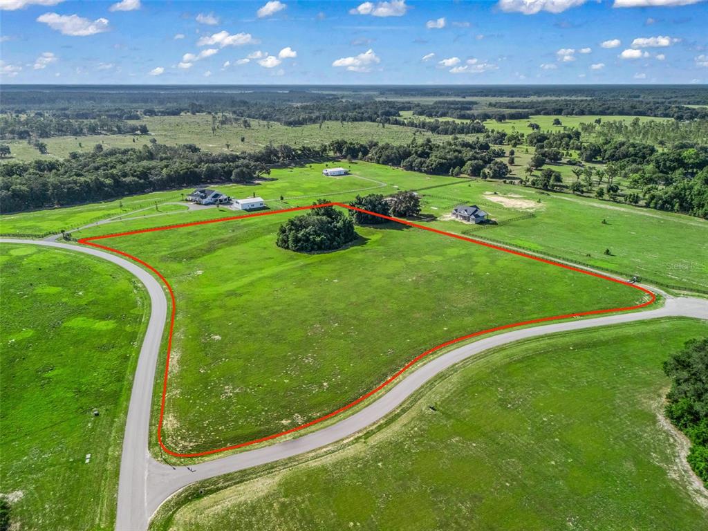 An aerial view shows a large, grassy, undeveloped lot outlined in red along a road — 0 NE 54TH TERRACE, ANTHONY, FL
