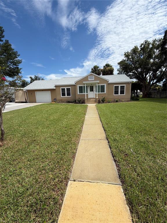 A single-story tan house with a white front door and a concrete walkway — 207 E HALIFAX AVENUE, OAK HILL, FL