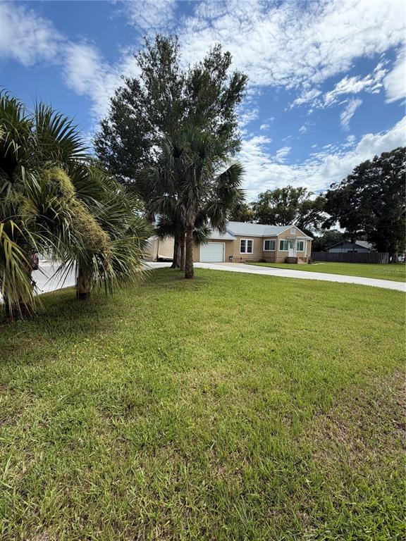 A single-story house with a white garage and palm trees sits on a grassy lawn — 207 E HALIFAX AVENUE, OAK HILL, FL