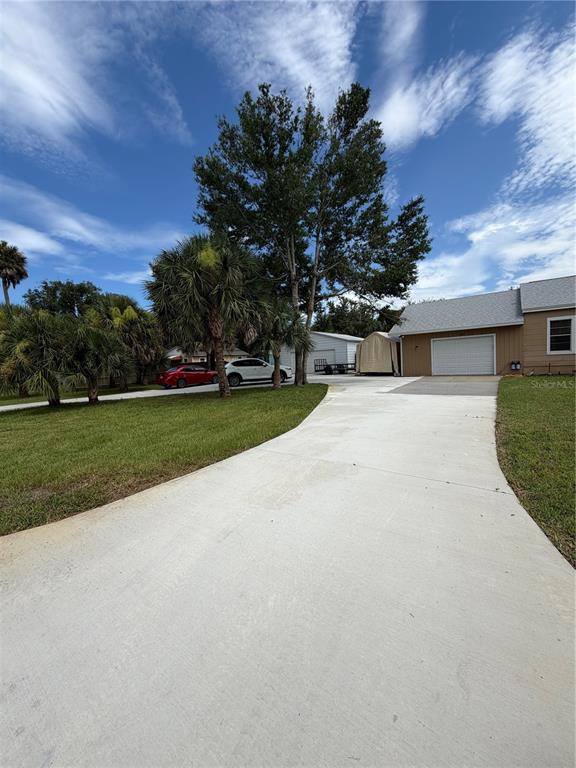 A concrete driveway leads toward a house with a garage and a detached carport — 207 E HALIFAX AVENUE, OAK HILL, FL