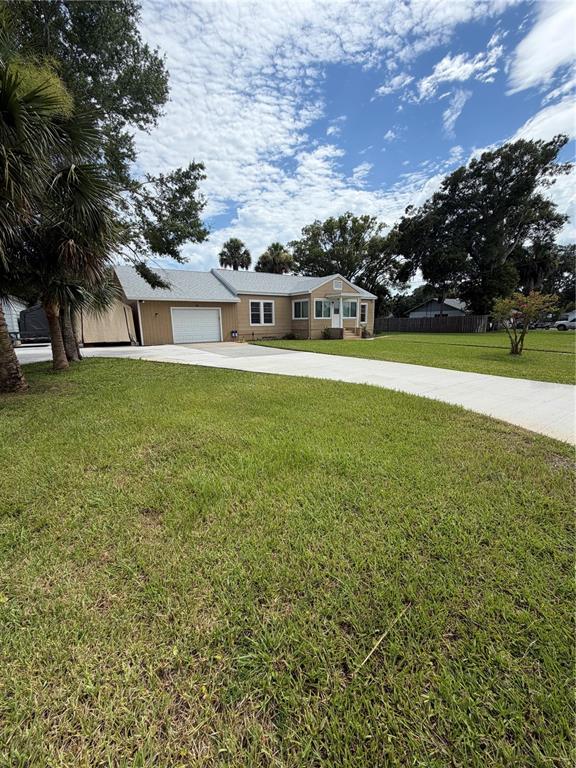 A tan single-story house with a white garage door and a concrete driveway — 207 E HALIFAX AVENUE, OAK HILL, FL