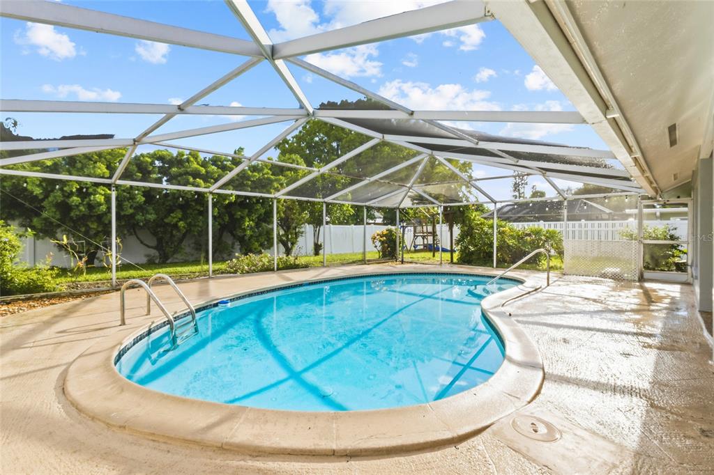 A screened-in swimming pool with a concrete deck and a white fence in the background — 7303 11TH AVENUE W, BRADENTON, FL