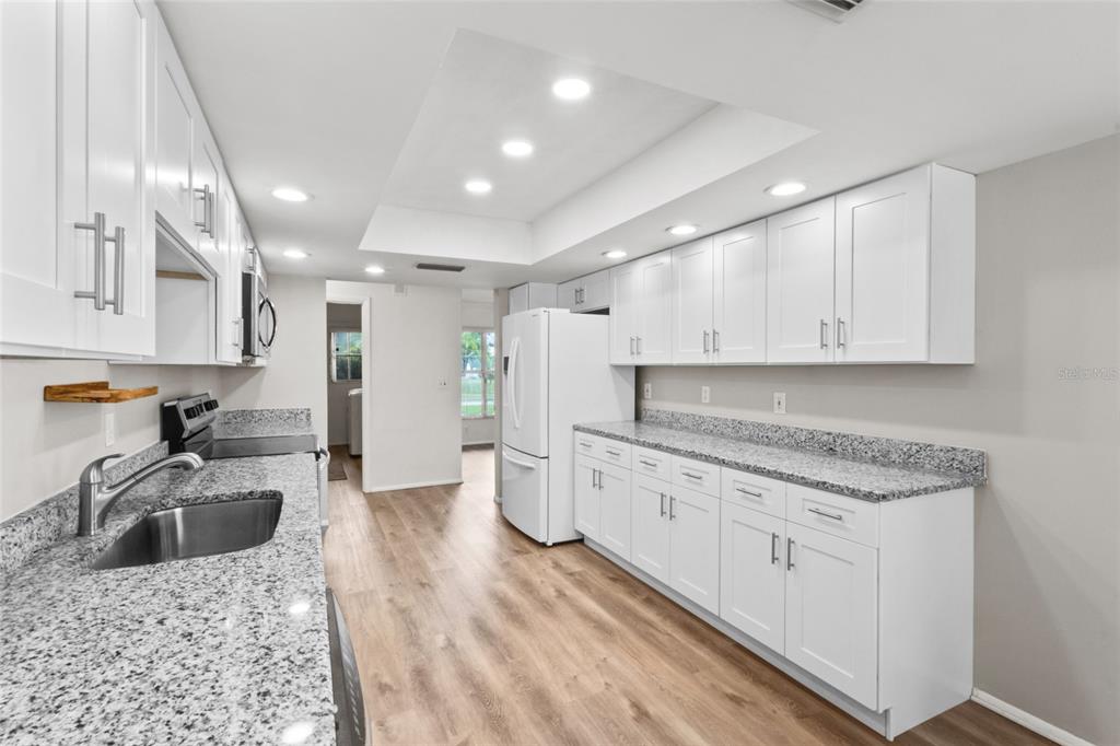 A kitchen with white cabinets, granite countertops, stainless steel sink, and light wood-look flooring — 7303 11TH AVENUE W, BRADENTON, FL