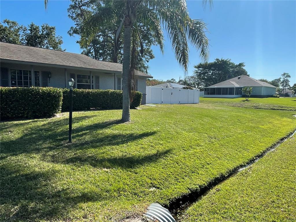 A view of a grassy yard with a house, palm tree, and white privacy fence — 2081 SW GEMINI LANE, PORT ST LUCIE, FL