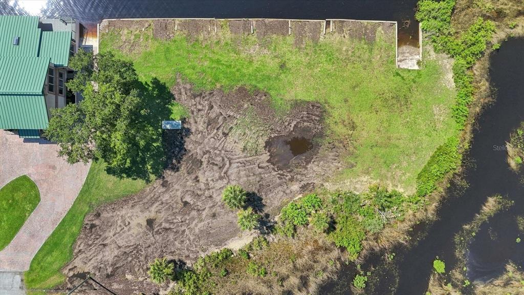 An aerial view shows a green-roofed house next to a cleared, muddy waterfront lot — 3190 INDIAN GULF LANE, HERNANDO BEACH, FL