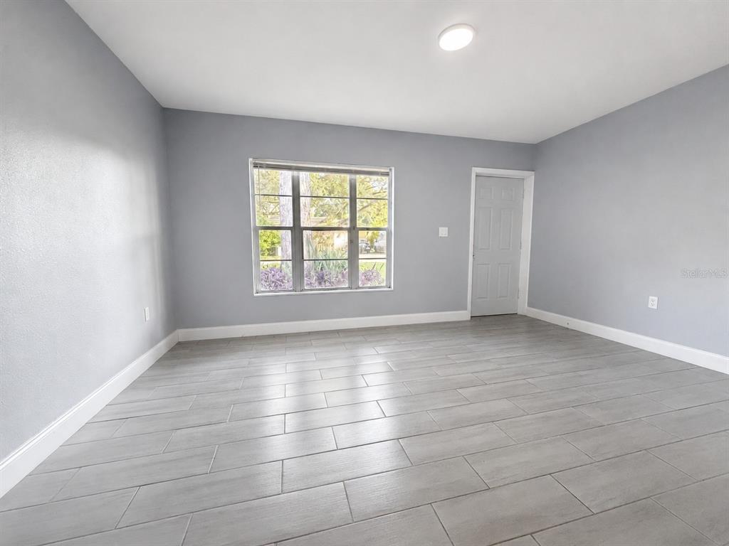 An empty room with gray walls, light-colored tile flooring, a window, and a white door — 6007 CORSON AVENUE, NEW PORT RICHEY, FL