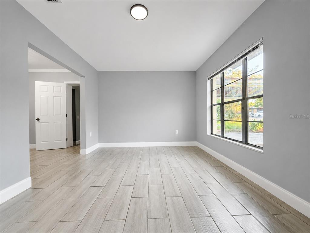 An empty room features light gray walls, white trim, and light wood-look tile flooring — 6007 CORSON AVENUE, NEW PORT RICHEY, FL