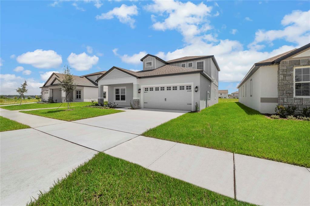 A two-story suburban house with a white garage and a green lawn under a sky — 3384 CHINOTTO DRIVE, LAKE ALFRED, FL
