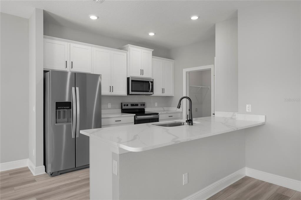 A modern kitchen features white cabinets, stainless steel appliances, and a white marble-look countertop island — 3384 CHINOTTO DRIVE, LAKE ALFRED, FL